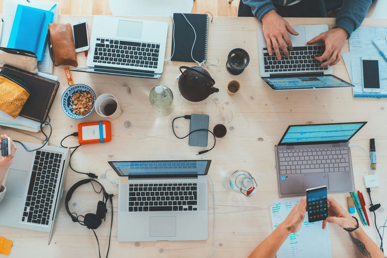 Blick von oben auf einen Tisch mit mehreren Laptops, Notizbüchern und Kaffeebechern – Co-Working im Startup-Setup